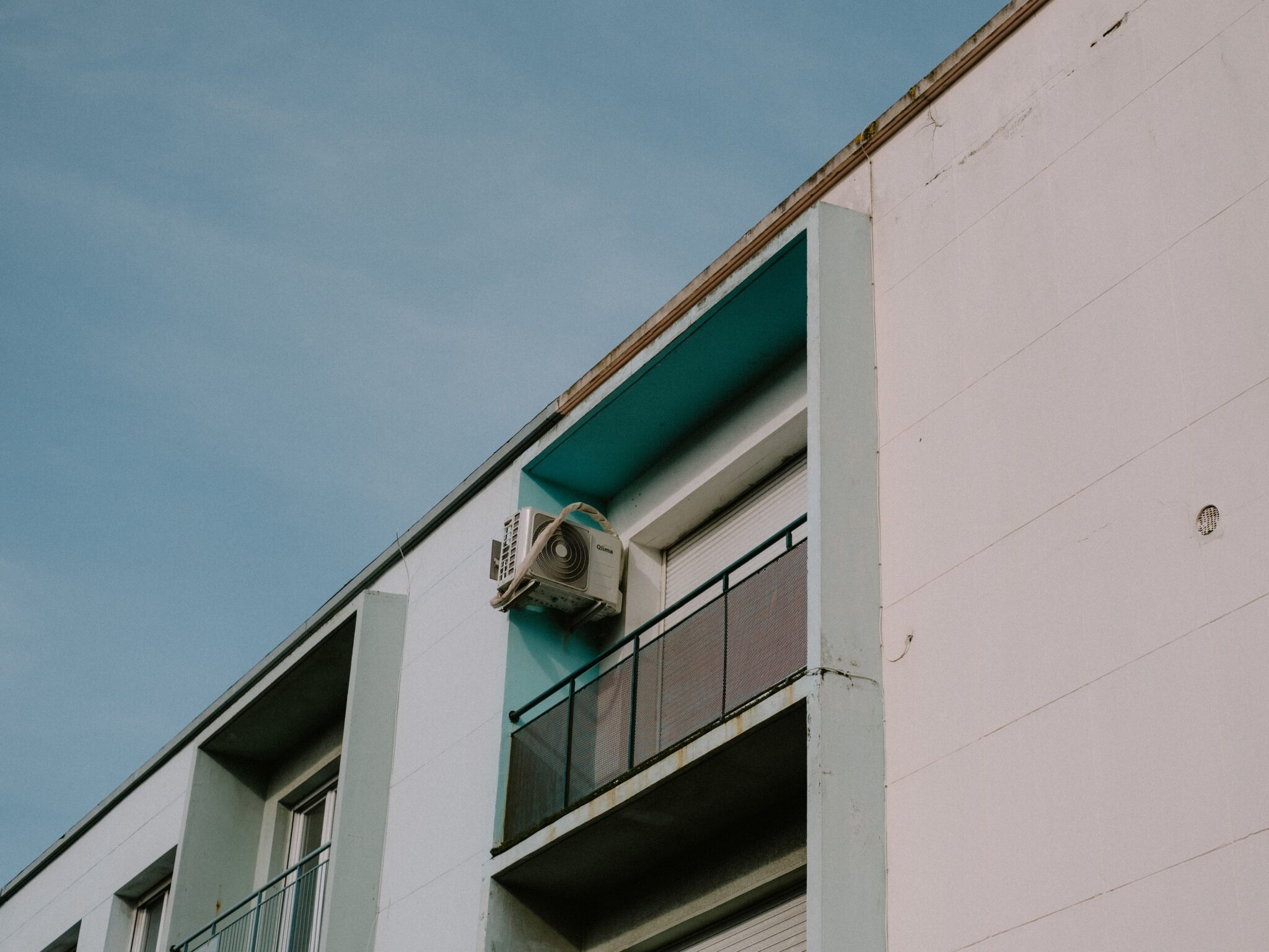 Wall-mounted AC condenser on the side of an apartment balcony